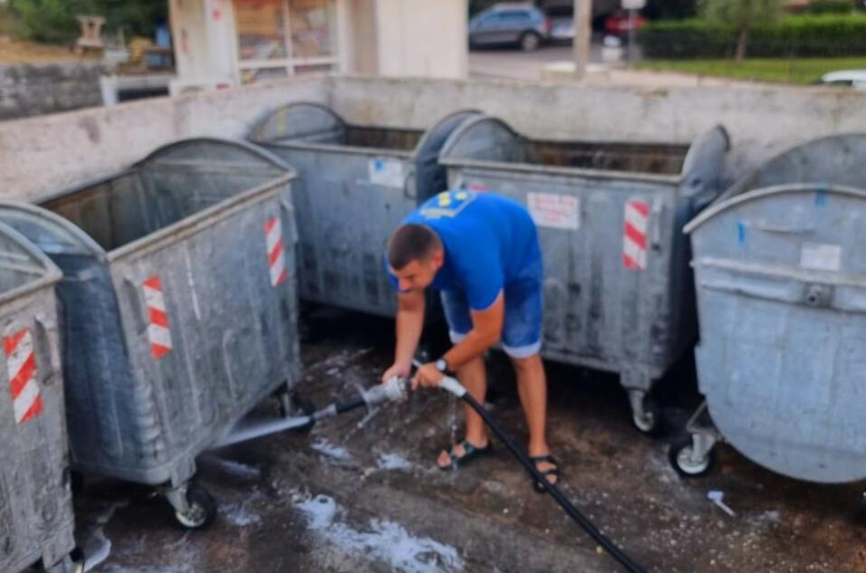 Мужчина моет мусорный контейнер